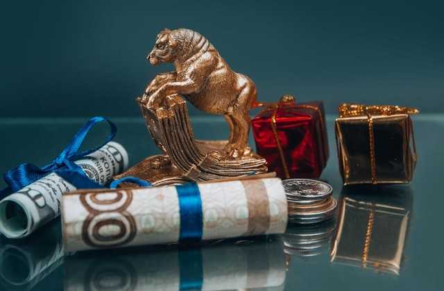 На столе лежат свёрнутые в трубочки и украшенные синей лентой банкноты, как один из способов, как оригинально подарить деньги