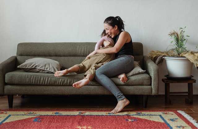 Мама с дочкой радостно обнимаются на диване, потому что узнали, что такое семейный бюджет и могут начать экономить
