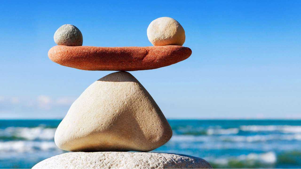 Фигура из камней в виде уравновешенных весов на фоне моря как метафора финансового успеха через гармонию
