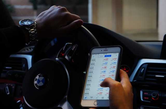 Мужчина едет в машине и одновременно проверяет в телефоне, как купить криптовалюту в Украине