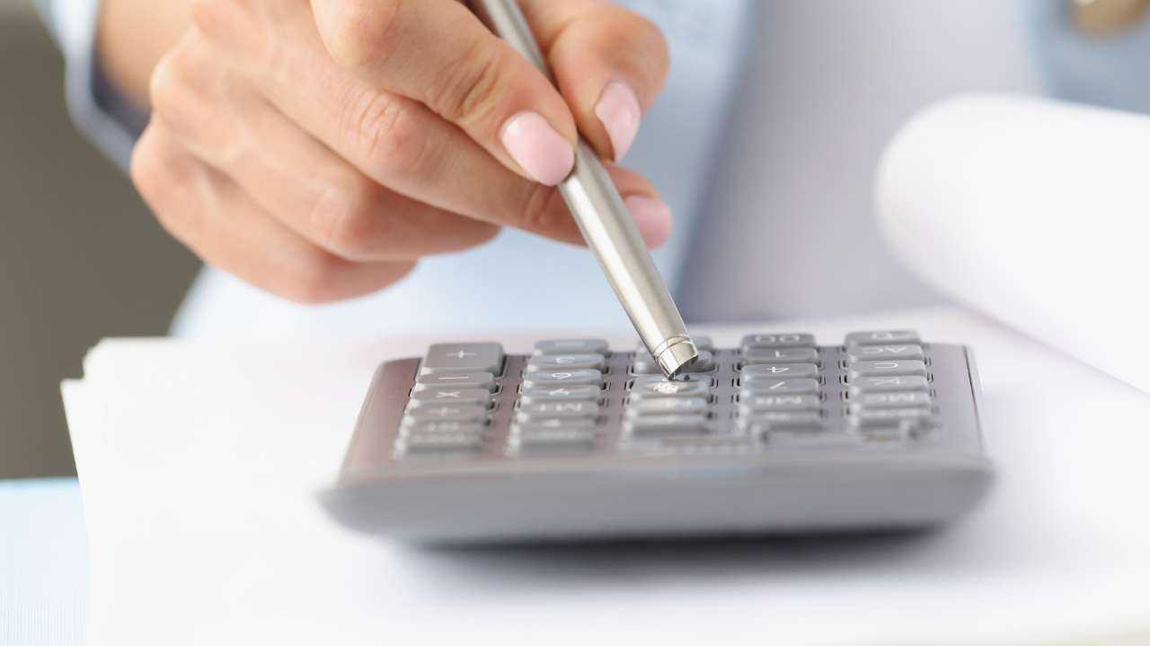 Женщина при помощи ручки на калькуляторе просчитывает свой бюджет, т.к. хочет улучшить свое финансовое положение