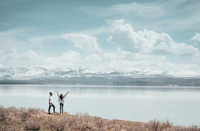 Молодая пара стоит на берегу озера и радуется, что узнали, как начать путешествовать без денег