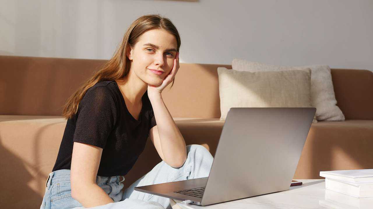 Женщина улыбается и смотрит в ноутбук, исследуя способы получения пассивного дохода в интернете