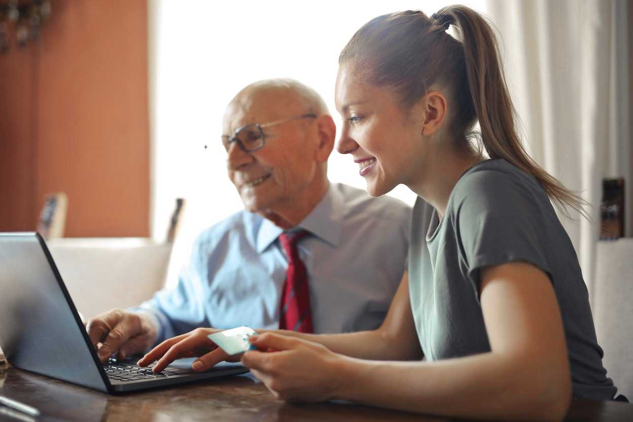 Млада жена и стар мъж седят пред лаптоп