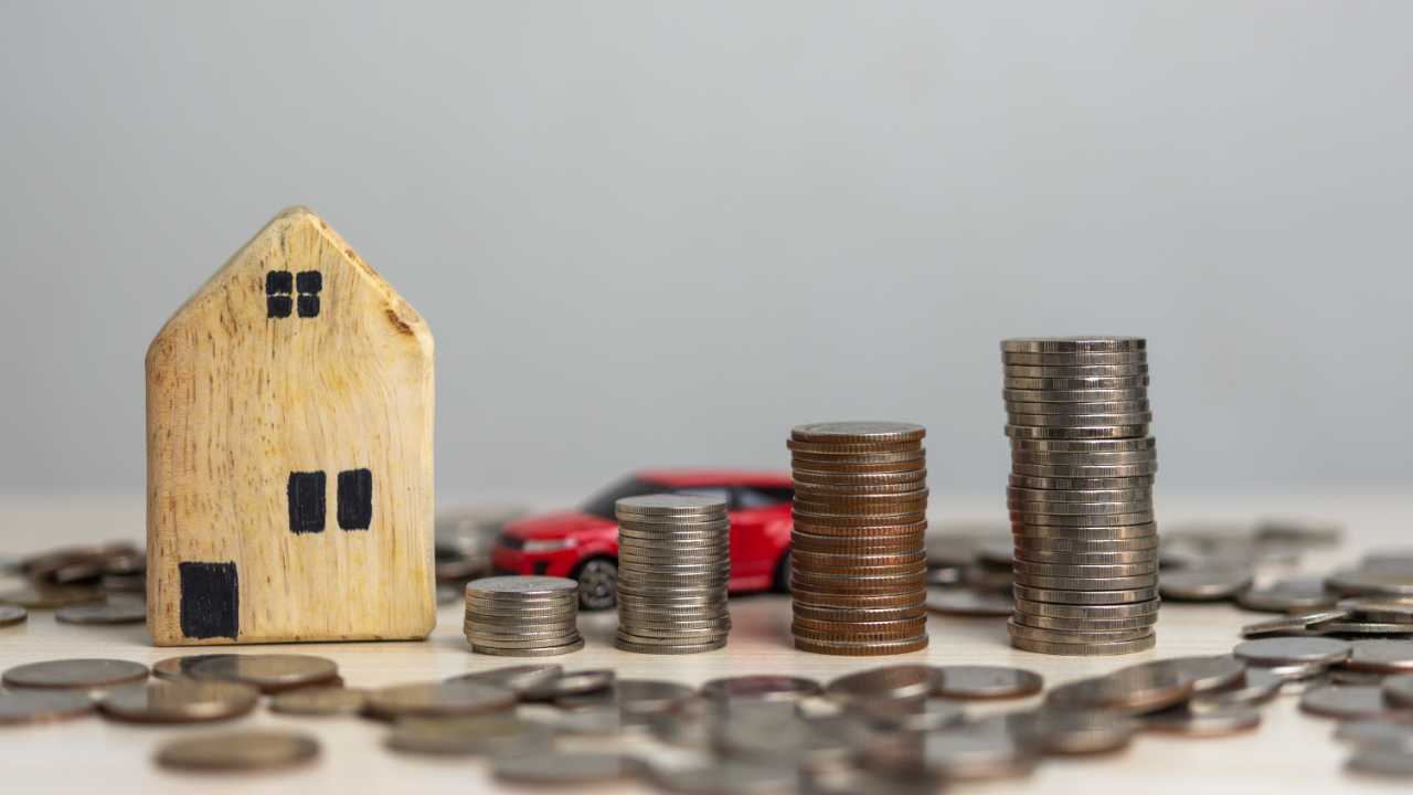 A wooden toy house, four columns of coins arranged in a row, lying coins and a red toy car represent a home credit cash loan