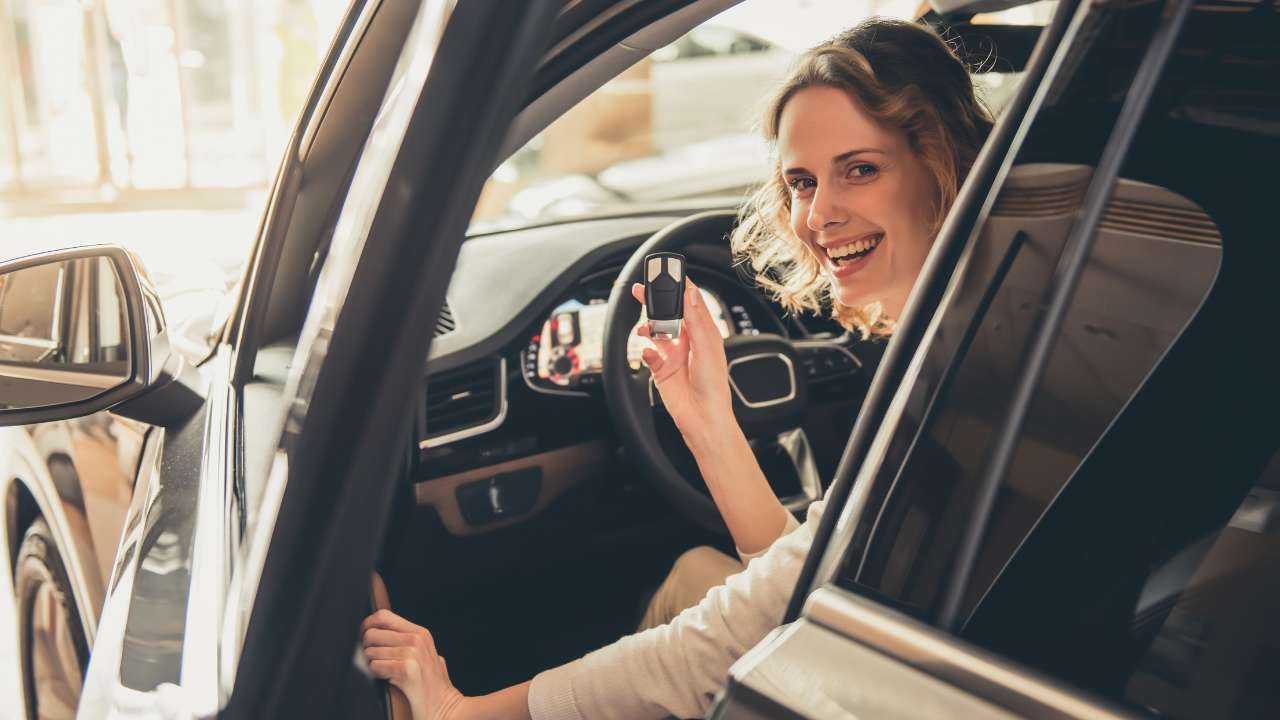 Sieviete sēž auto ar atslēgu un smaida, jo ir efektīvi izplānojusi automašīnas iegādi